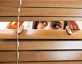 Brown-eyed girl peeps fearfully through venetian blinds