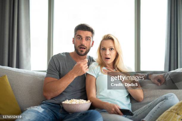 shocked mid adult couple watching a movie. - couple in surprise stock pictures, royalty-free photos & images