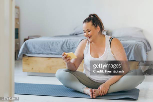 exercice à la maison: une femme de taille plus au cours d’une séance d’entraînement à domicile suivant sur le programme de remise en forme en ligne - curvy woman photos et images de collection