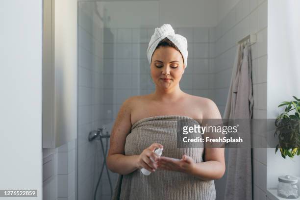 mooie overgewicht vrouw gewikkeld in een handdoek toepassing van body lotion na het hebben van een douche - beautiful woman body stockfoto's en -beelden