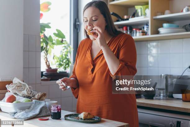 plus size woman eating a croissant and jam for breakfast - voluptuous stock pictures, royalty-free photos & images