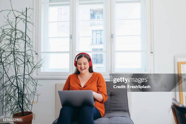 happy plus size mujer usando auriculares viendo algo divertido en su pc portátil - curvy woman fotografías e imágenes de stock