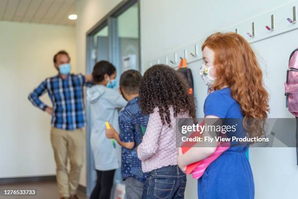 de leraar die een gezichtsmasker draagt begroet basisschoolleerlingen in gang buiten klaslokaal op school - school rules stockfoto's en -beelden