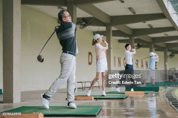 亞洲中國活躍高級男子高爾夫球手發球和擺動他的潛水高爾夫球杆在高爾夫練習場與家人。 - driving range 個照片及圖片檔