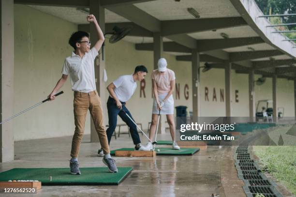 asian chinese young boy practicing golf in driving range with his parents during raining - driving range stock pictures, royalty-free photos & images