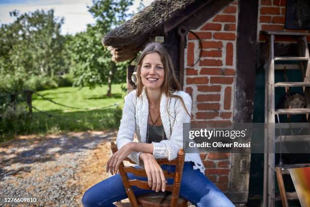 smiling woman sitting on wooden chair on a farm - fachwerk stock-fotos und bilder