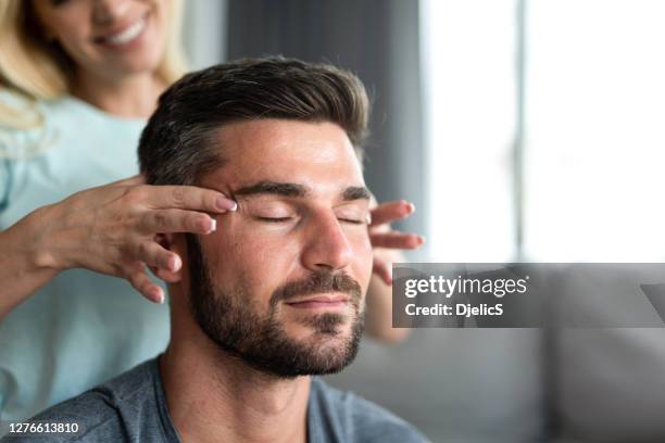 young man receiving a relaxing temple massage from wife - head massage stock pictures, royalty-free photos & images