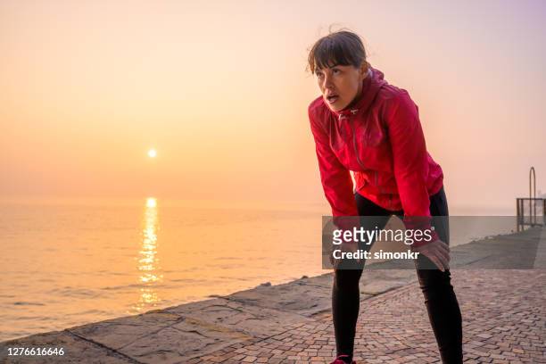 mid adult woman taking a break while exercising outdoors - hand on knee stock pictures, royalty-free photos & images