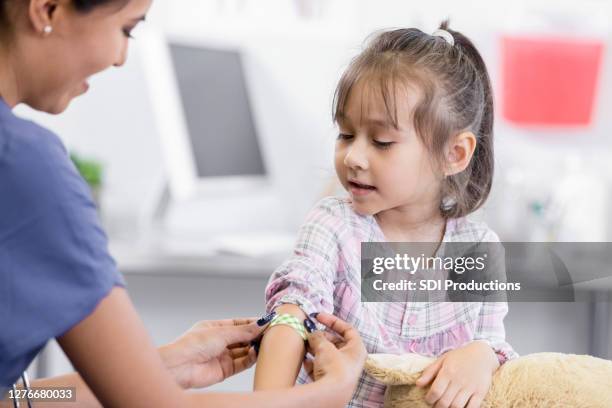 cheerful nurse puts adhesive bandage on preschool girl's arm - applying bandaid stock pictures, royalty-free photos & images