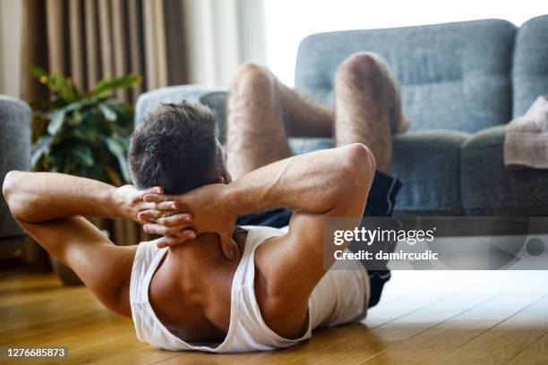 young athletic man doing sit-ups in the living room - abs stock pictures, royalty-free photos & images