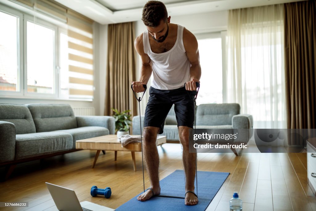 Ung atletisk man träning med stretching band hemma