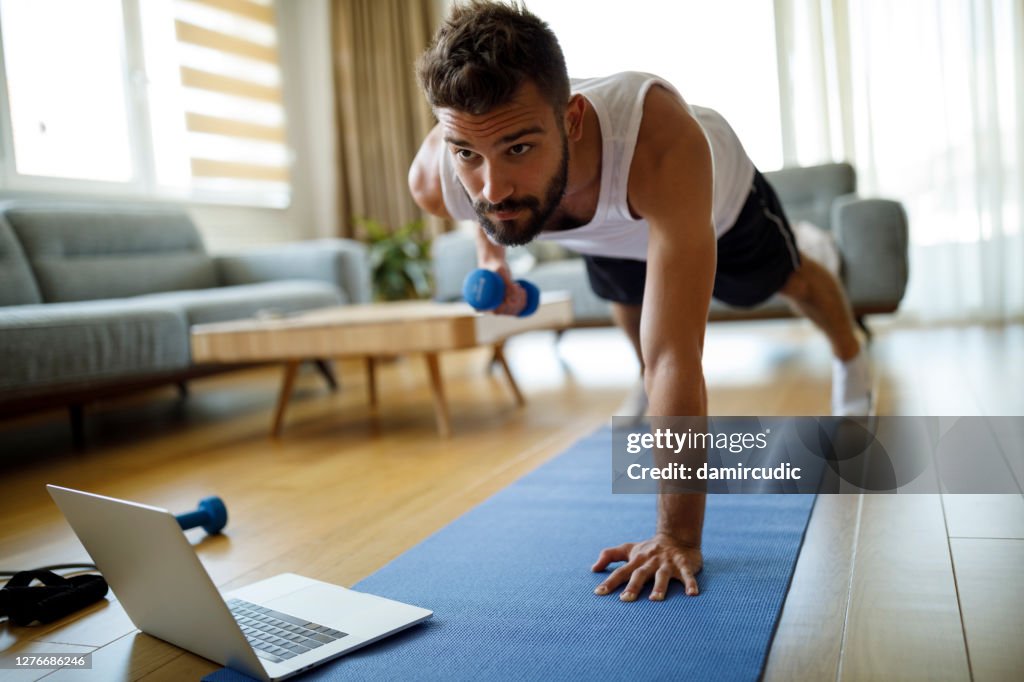 Joven usando computadora portátil y haciendo ejercicio en casa