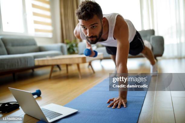 joven usando computadora portátil y haciendo ejercicio en casa - exercise at home fotografías e imágenes de stock