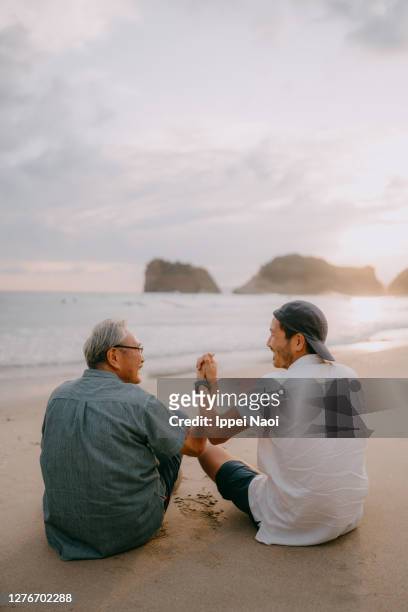 senior father and son holding hands on beach at sunset - incoraggiamento foto e immagini stock