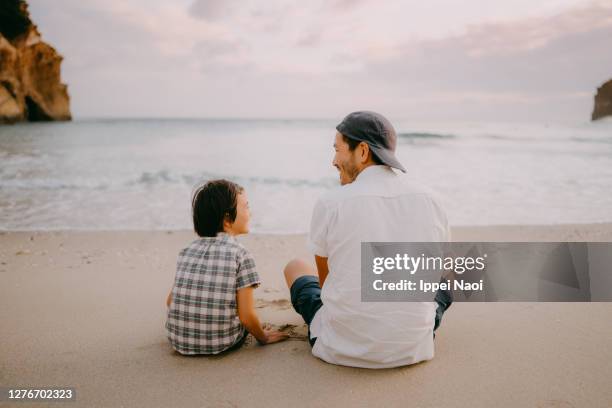 father and daughter sitting on beach at sunset - children sitting back foto e immagini stock