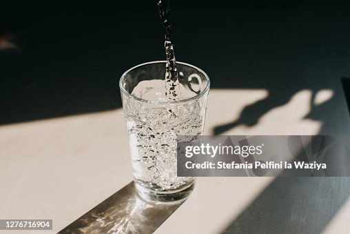 Water being poured in a glass of water that cast a beautiful shadow on a white kitchen countertop Water being poured in a glass of water that cast a beautiful shadow on a white kitchen countertop
