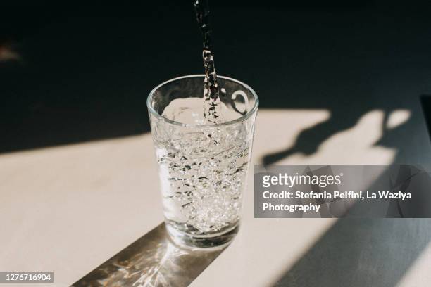 water being poured in a glass of water that cast a beautiful shadow on a white kitchen countertop - drinking glass foto e immagini stock