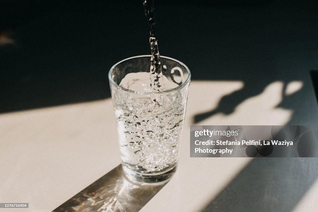 Water being poured in a glass of water that cast a beautiful shadow on a white kitchen countertop