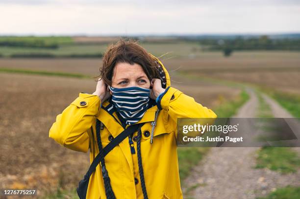 woman putting on neck gaiter in countryside - snood headwear stock pictures, royalty-free photos & images