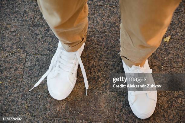 the girl's feet are in new white sneakers and jeans, one lace is untied. a woman in athletic shoes is walking on the sidewalk. fashionable and stylish lifestyle. - untied shoelace stock pictures, royalty-free photos & images