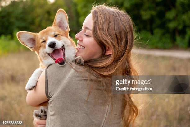 ritratto: giovane donna con cucciolo di corgi ridente, sfondo della natura - abbracciare una persona foto e immagini stock