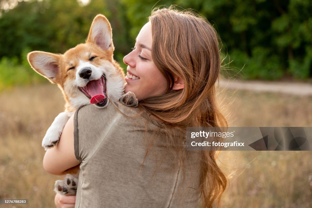 Portrait: young woman with laughing corgi puppy, nature background