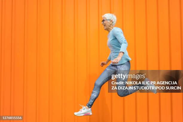 donna anziana felice che salta su sfondo arancione. - jumping foto e immagini stock