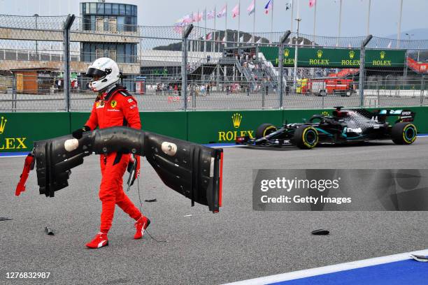 Sebastian Vettel of Germany and Ferrari retrieves his front wing from the track after crashing as Lewis Hamilton of Great Britain driving the...