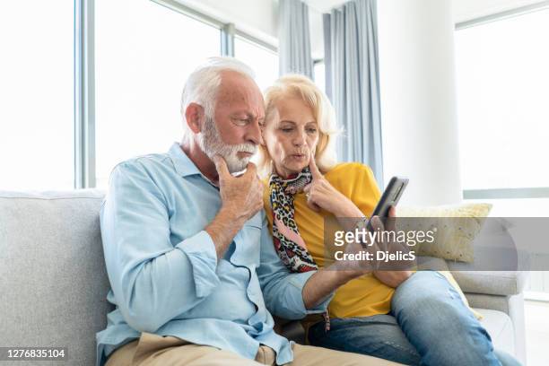 worried senior couple looking at phone in the living room - cell phone confused stock pictures, royalty-free photos & images