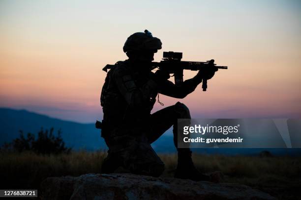 silhouet van een knielende turkse militair die bij doel bij zonsondergang ontspruit - counter terrorism stockfoto's en -beelden