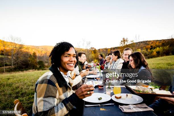 cheerful woman enjoying dinner party in field with friends - country style stock-fotos und bilder