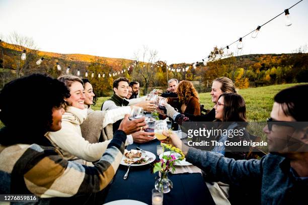 group of friends toasting at outdoor dinner party in field - outdoor party imagens e fotografias de stock