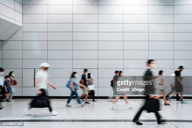 blurred motion of a crowd of busy commuters with protective face mask walking through platforms at subway station during office peak hours in the city - hauptverkehrszeit stock-fotos und bilder