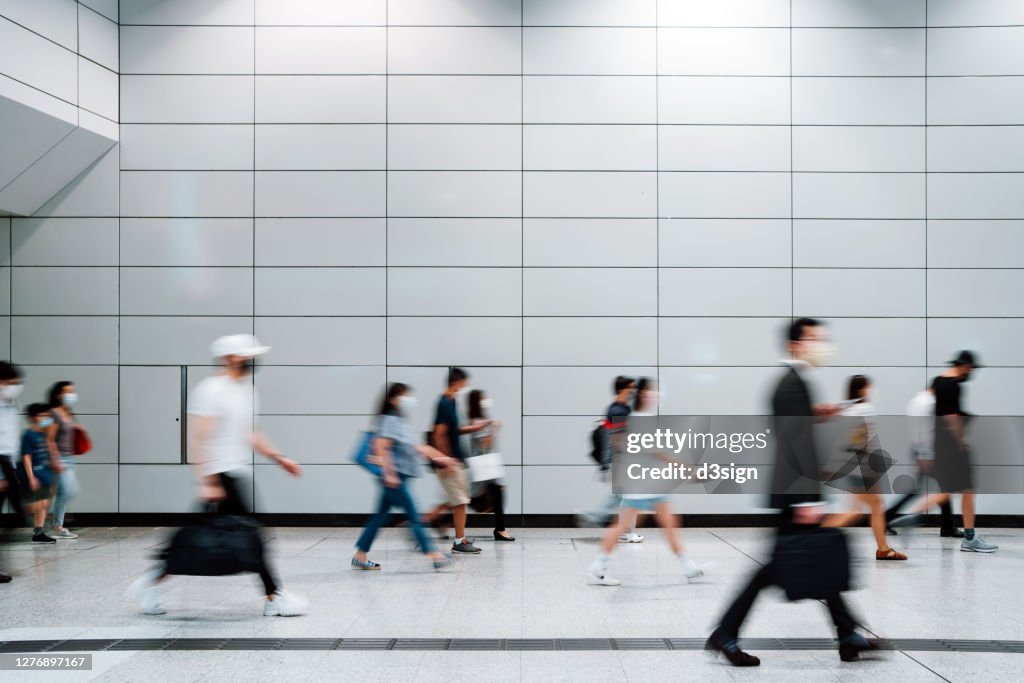 Blurred motion of a crowd of busy commuters with protective face mask walking through platforms at subway station during office peak hours in the city
