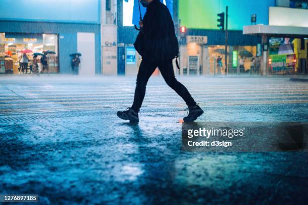 silhouette of a man carrying umbrella walking in downtown city street against the reflection of glowing neon lights and city buildings in heavy rain at night - torrential rain stock pictures, royalty-free photos & images