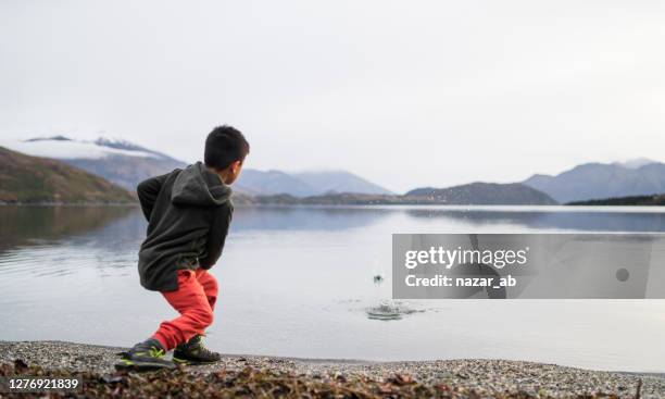 jong geitje dat stenen in meer overslaat. - boy throwing stockfoto's en -beelden