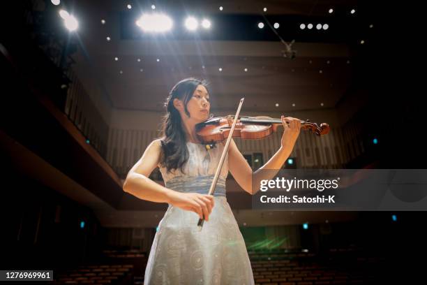 female violinist playing the violin in concert hall - professional musician stock pictures, royalty-free photos & images