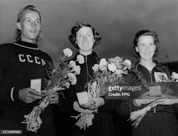 Soviet athlete Aleksandra Chudina , New Zealand athlete Yvette Williams , and British athlete Shirley Cawley, each holding a bouquet of flowers and...