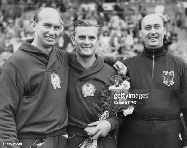 Hungarian athlete Imre Nemeth with his arm around Hungarian athlete Jozsef Csermak , who holds a bouquet of flowers, and German athlete Karl Storch ,...