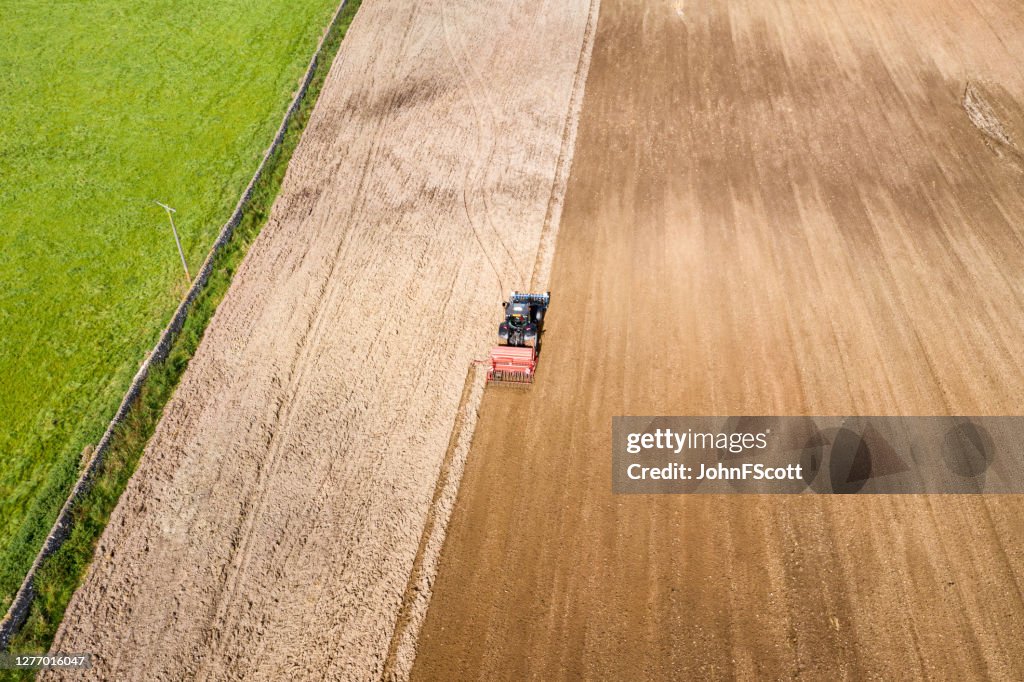 Aerial rear view of a tractor being used to pull a seed drill on a Scottish farm on a late summer day