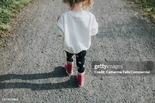 little girl on a gravel path walking in bright pink wellington boots - stepping stock pictures, royalty-free photos & images