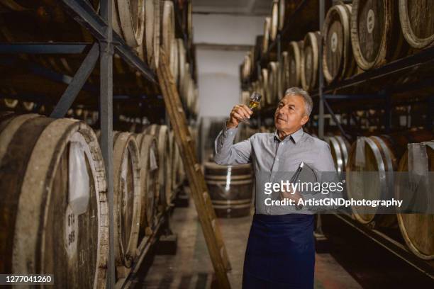 distillery manager is taking samples from the barrels and trying the whiskey - destilação imagens e fotografias de stock