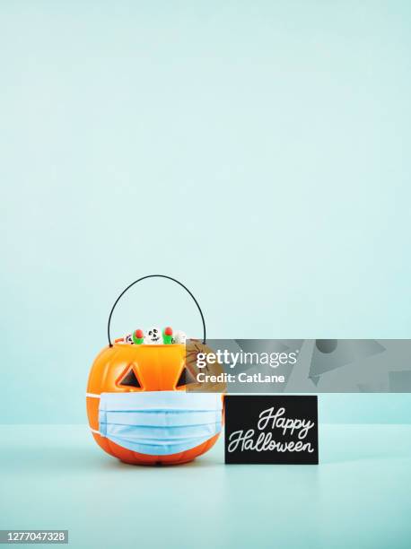 halloween background with jack o'lantern filled with candy wearing a face mask - safety month stock pictures, royalty-free photos & images