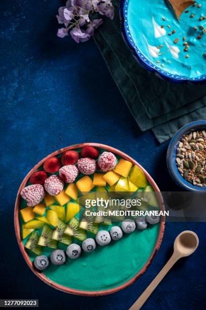 blue and green spirulina yogurt bowls breakfast with berries - yellow smoothie stock pictures, royalty-free photos & images