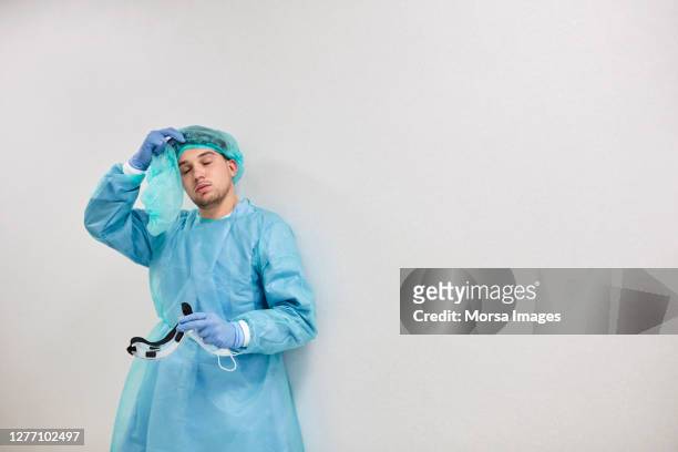 exhausted medical professional in blue coveralls during pandemic - removing surgical mask stock pictures, royalty-free photos & images
