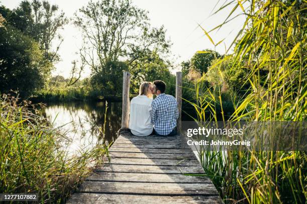 portrait of young couple kissing on dock overlooking pond - kissing mouth stock pictures, royalty-free photos & images