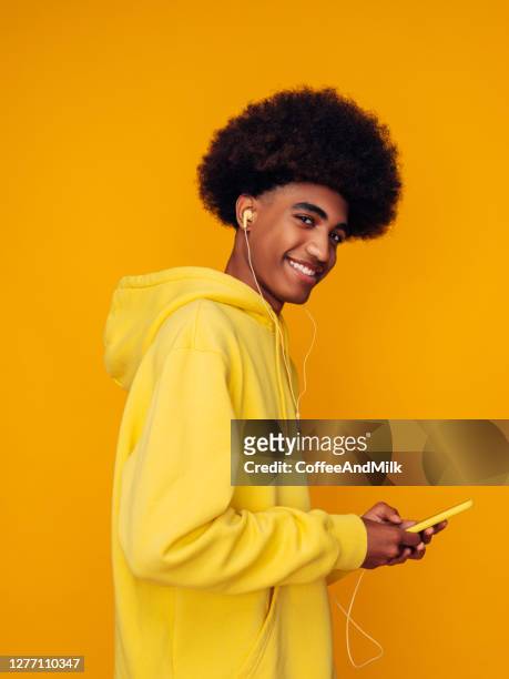 孤立した黄色の背景の上に立ってパーカーを着たアフリカの髪型を持つアフリカ系アメリカ人男性 - headphones isolated ストックフォトと画像