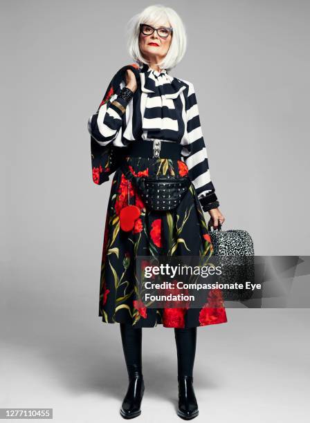 senior woman holding suitcase wearing stylish clothes - rode rok stockfoto's en -beelden