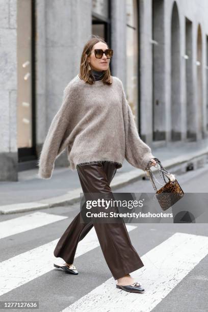 Influencer Annette Weber wearing brown leather pants and a fuzzy oversized beige pullover by Brunello Cucinelli, a varenne leopard print clutch by...