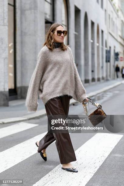 Influencer Annette Weber wearing brown leather pants and a fuzzy oversized beige pullover by Brunello Cucinelli, a varenne leopard print clutch by...